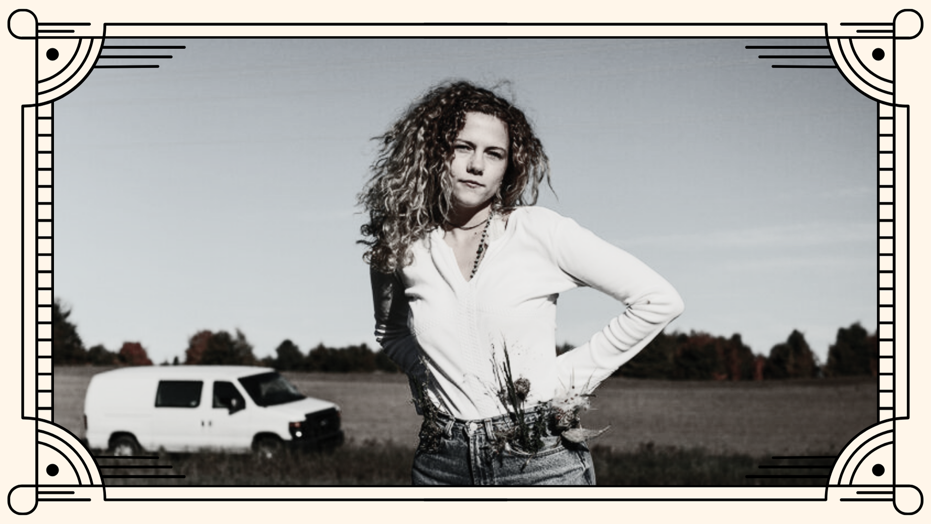 Musician i.am.james in a field with a white van behind her and flowers in her pocket.